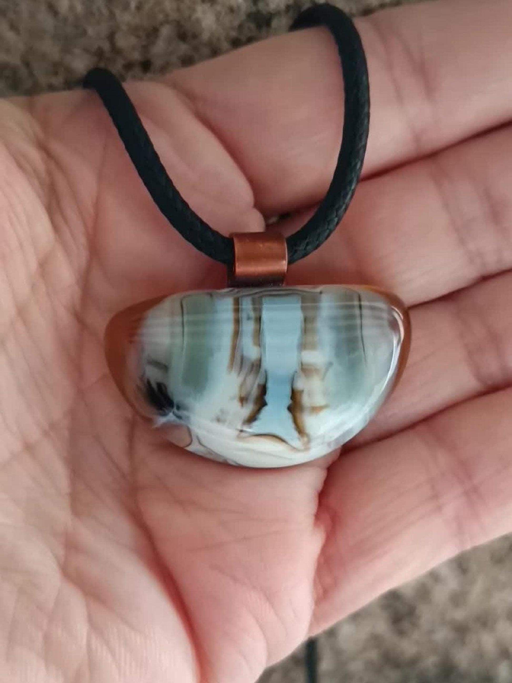 Fused glass pendant on a grunge black cord necklace with copper bail; orange bottom with blue-green swirls and brown lines.
