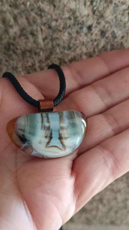Fused glass pendant on a grunge black cord necklace with copper bail; orange bottom with blue-green swirls and brown lines.